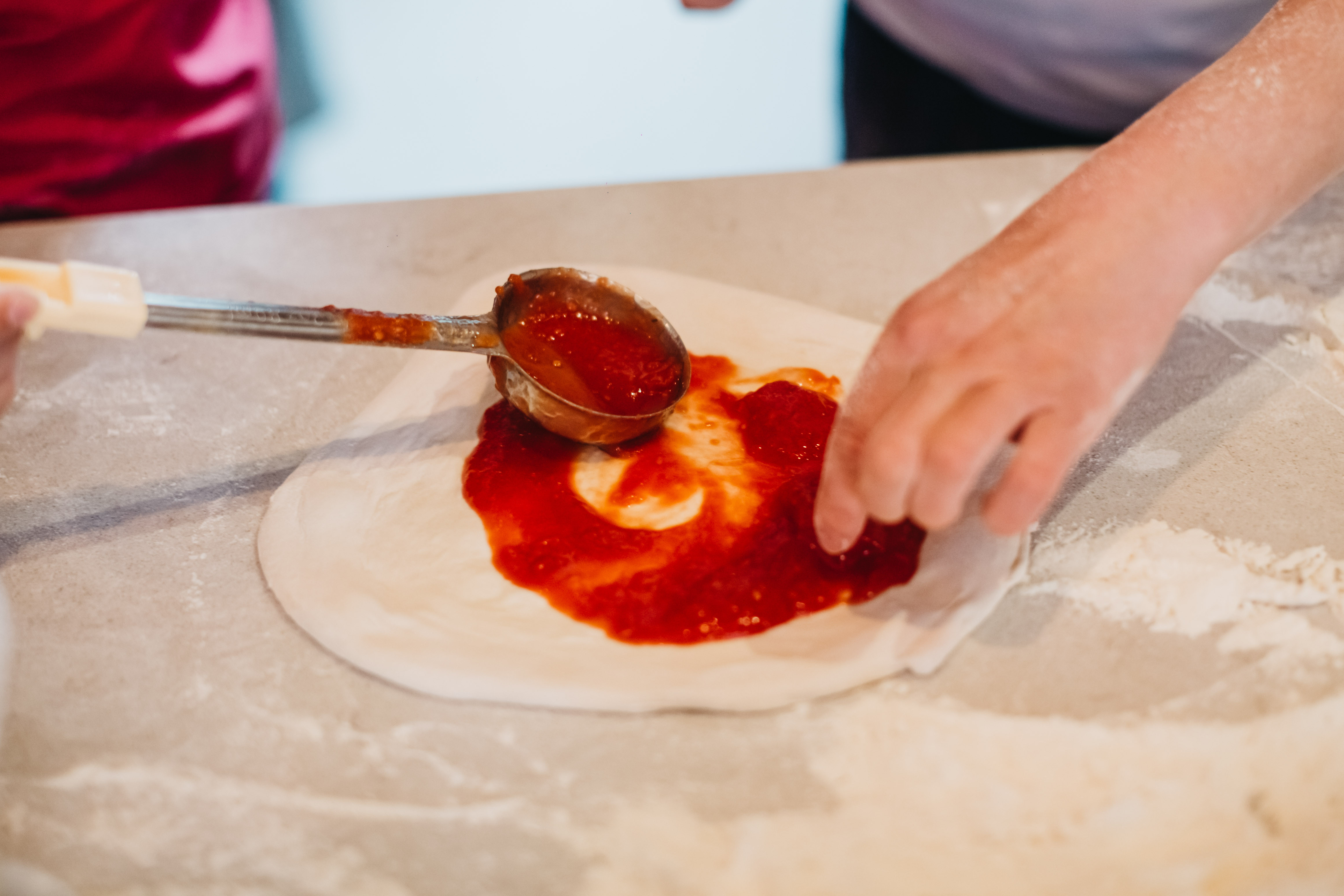 Spreading red sauce on a pizza base using a metal ladle